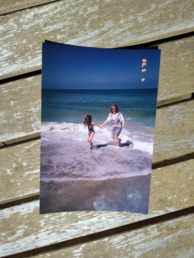 A woman and a girl holding hands while playing in the waves at the beach on a sunny day.